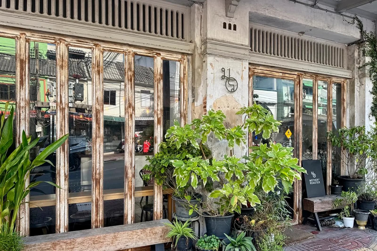 Potted plants and old wooden shophouse doors outside a Mother Roaster cafe in Bangkok