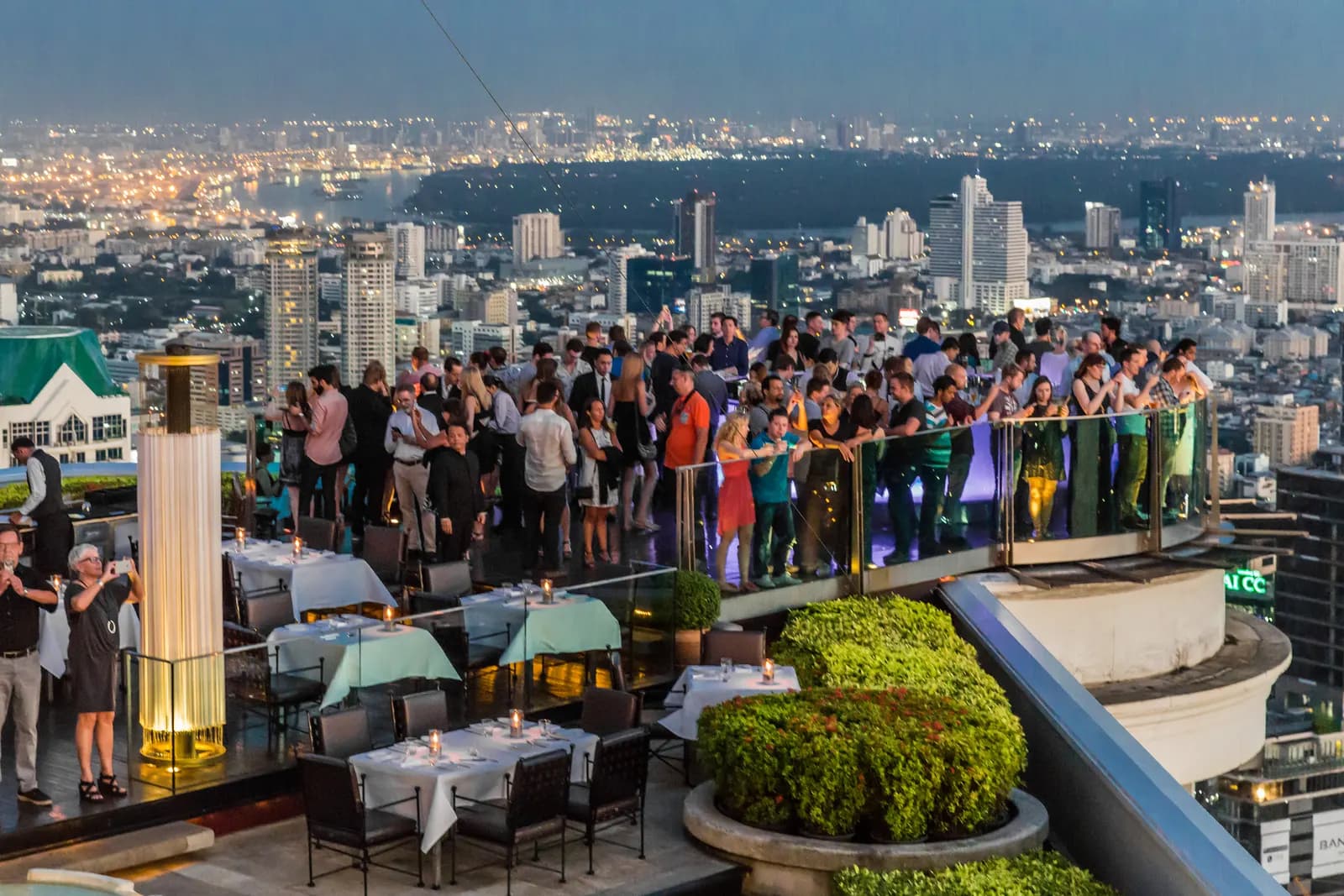 Sky Bar on the 64th floor of State Tower in Bangkok at dusk, with the city and the Chao Phraya River behind