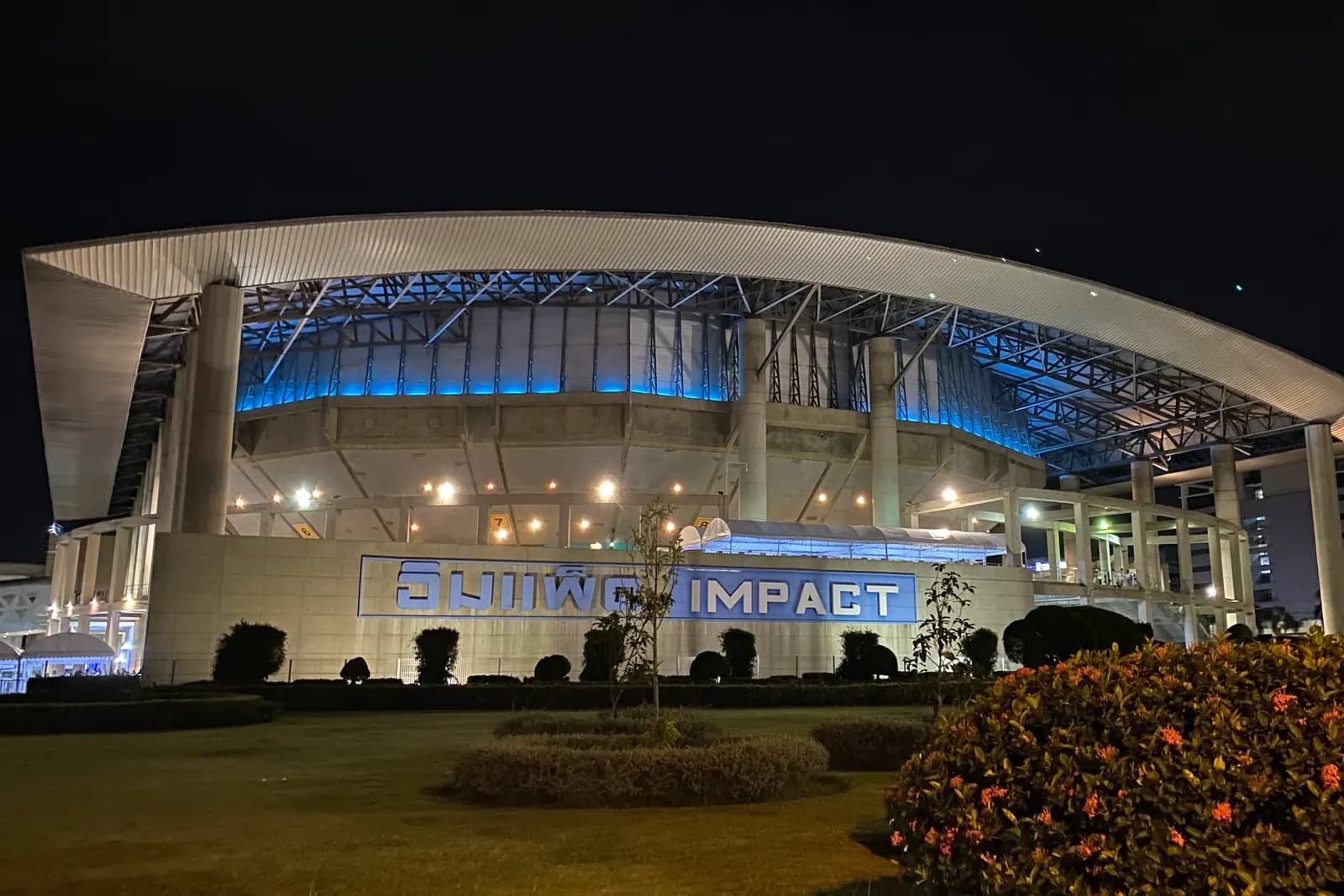 IMPACT Arena at Muang Thong Thani lit up at night, its curved roof over the IMPACT sign