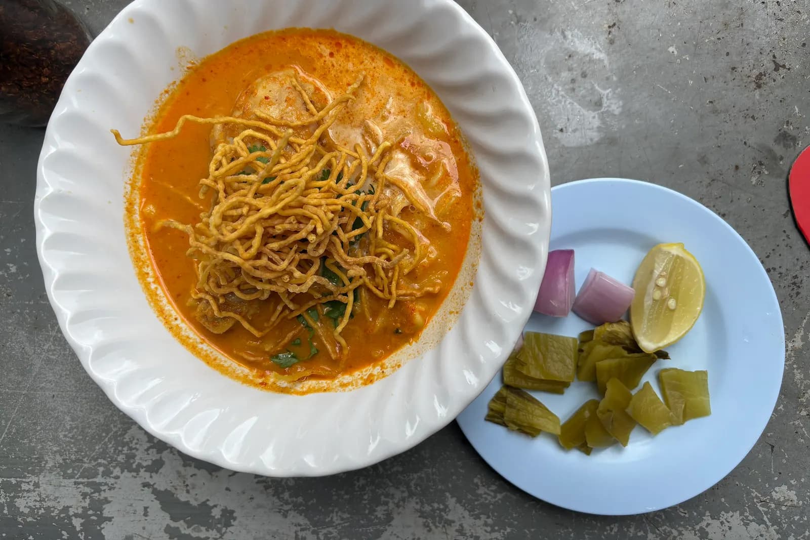 A bowl of khao soi topped with crispy noodles, with shallots, lime and pickled mustard greens on the side, at Khao Soi Khun Yai in Chiang Mai