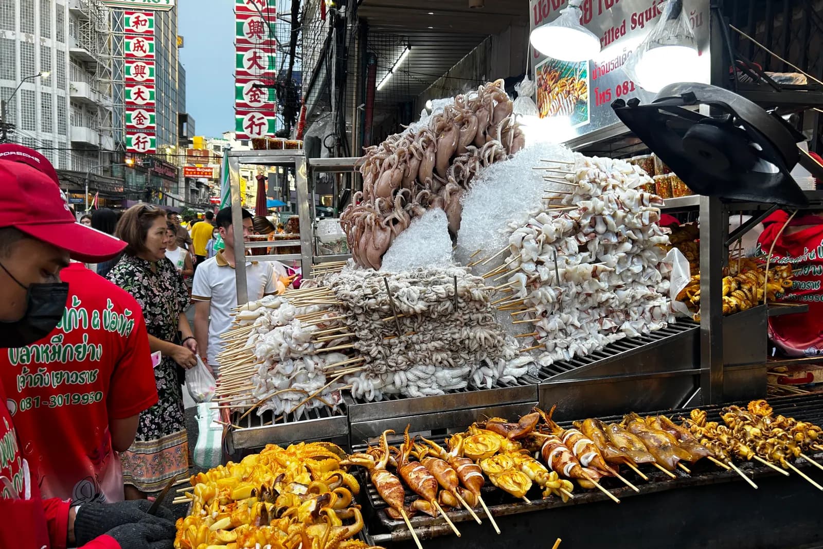 Squid and cuttlefish skewers on the grill at a stall on Yaowarat Road, under Chinatown's neon signs