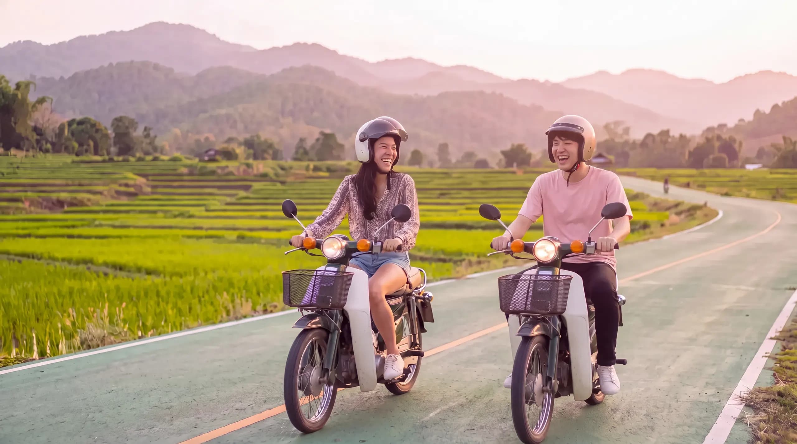 Two friends riding scooters past rice fields outside Chiang Mai