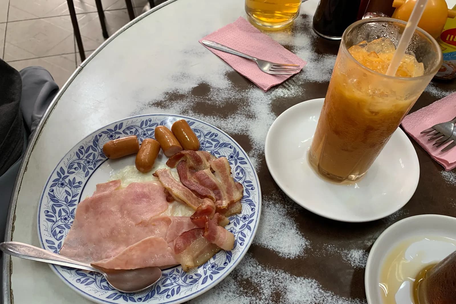 安乐园的早餐:蓝花盘里摆着火腿、培根、小香肠和煎蛋,旁边一杯泰式冰奶茶
