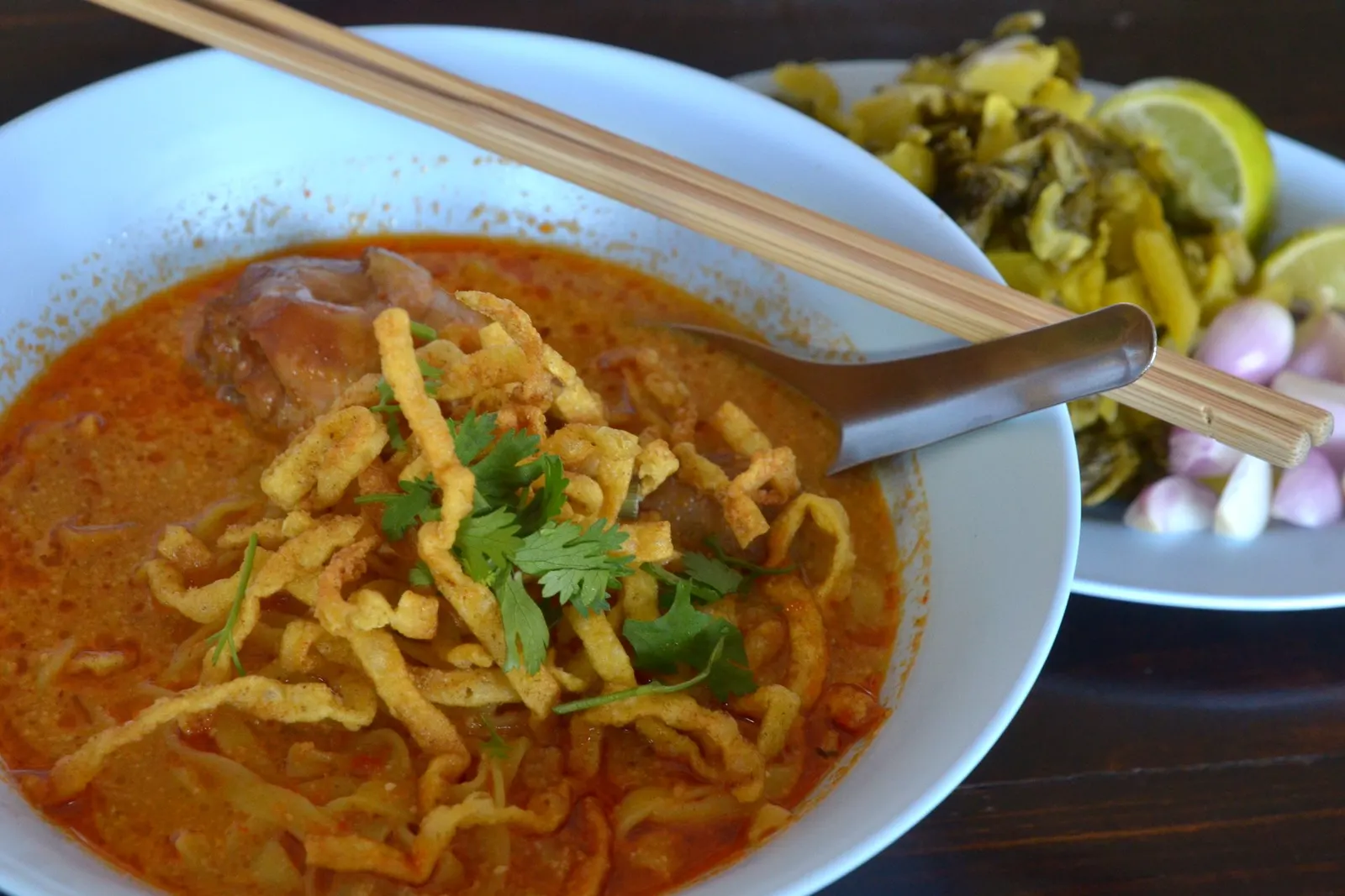 A bowl of khao soi with chicken, with pickled greens, shallots and lime on the side