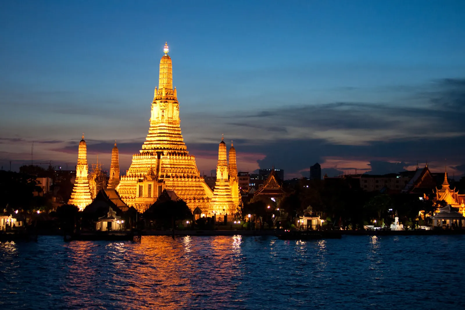 Wat Arun lit up at dusk across the Chao Phraya, the view the rooftop bars at Tha Tian look out on