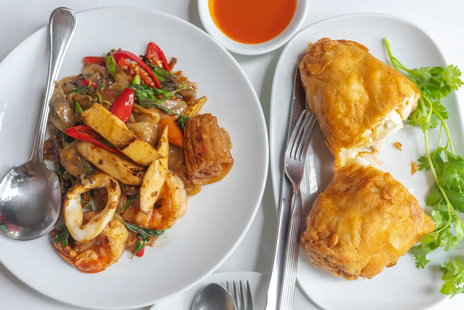 Drunken noodles with prawns and squid next to a crab omelette cut open, on the table at Jay Fai