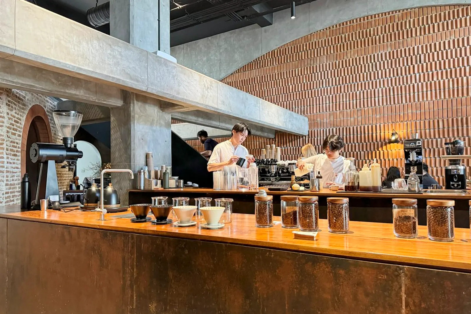 Baristas behind a long wooden bar lined with jars of beans at an Akha Ama Coffee shop in Chiang Mai