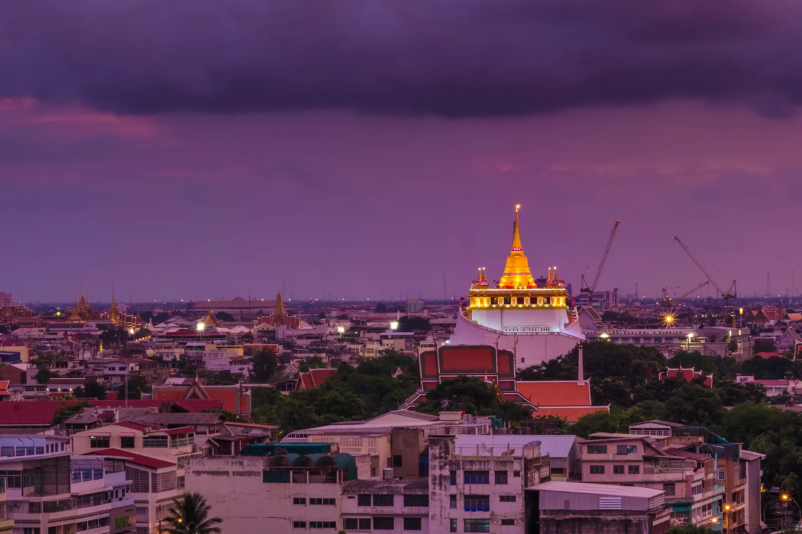 The Golden Mount at Wat Saket lit up at dusk above the rooftops of Bangkok's old town