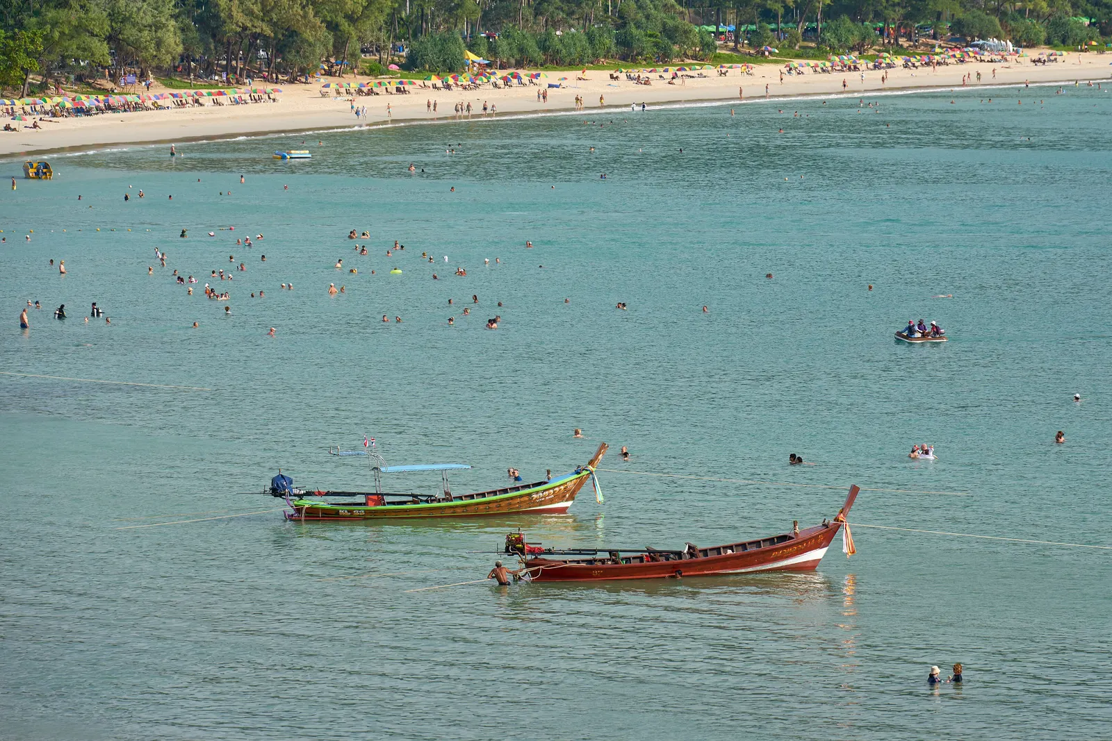 Swimmers and two longtail boats in calm water at Kata Beach, Phuket, on the morning of 1 December 2023